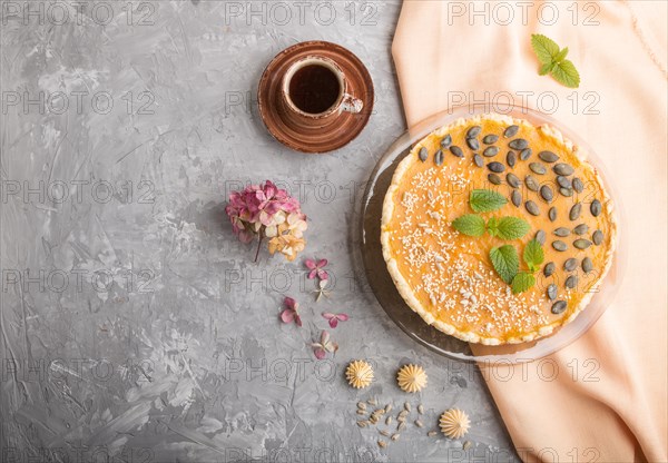 Traditional american sweet pumpkin pie decorated with mint, sesame and pumpkin seeds with cup of coffee on a gray concrete background. top view, flat lay, copy space