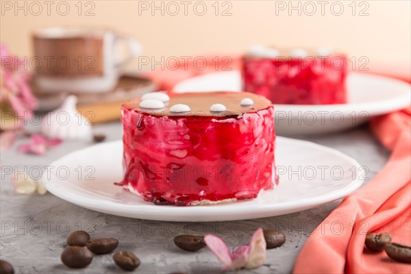 Red cake with souffle cream with cup of coffee on a gray concrete background and red textile. side view, close up. selective focus