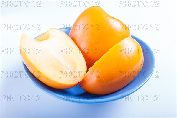 Ripe orange persimmon in a blue plate isolated on white background. closeup