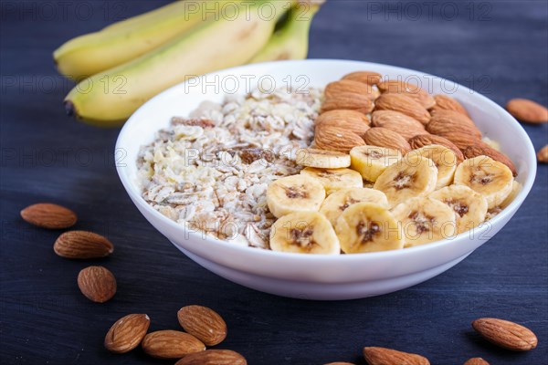 A plate with muesli, almonds, banana, sliced persimmon on a black wooden background. close up. copy space