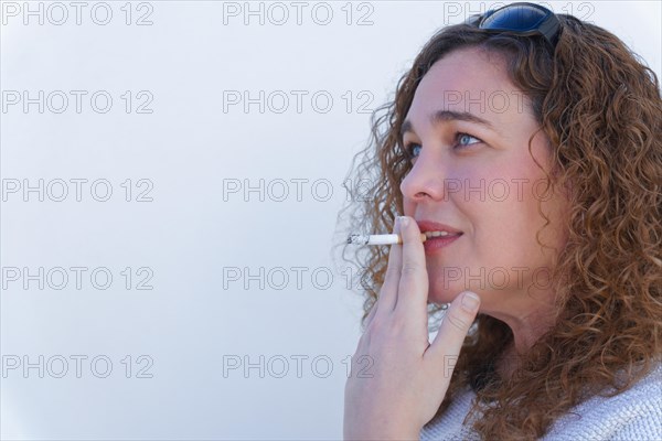 Attractive blue-eyed, curly-haired woman in profile smoking a cigarette with white background and copy space