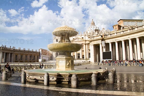 View of a fountain in St Peter's Square in the Vatican in front of the basilica under a cloudy sky