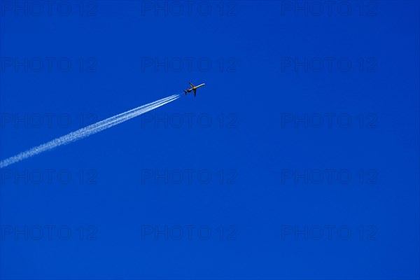 A passenger plane with vapour trail high in the blue sky