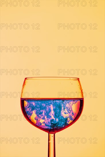 A wine glass filled with a vivid blue liquid, illuminated in red against a yellow background