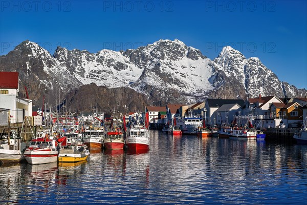Bunte Boote und Gebaeude vor schneebedeckten Bergen in einem Hafen, Im Hafen von Henningsvaer auf den Lofoten