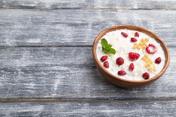 Rice flakes porridge with milk and strawberry in wooden bowl on gray wooden background. Side view, copy space, close up
