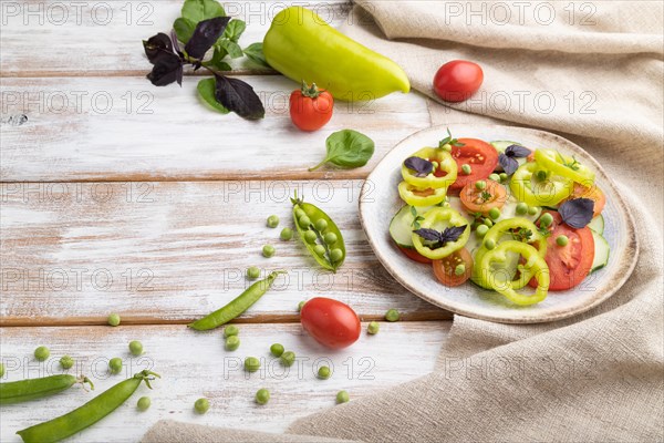Vegetarian salad from green pea, tomatoes, pepper and basil on white wooden background and linen textile. Side view, copy space