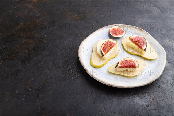 Summer appetizer with pear, cottage cheese, figs and honey on ceramic plate on a black concrete background. Side view, copy space