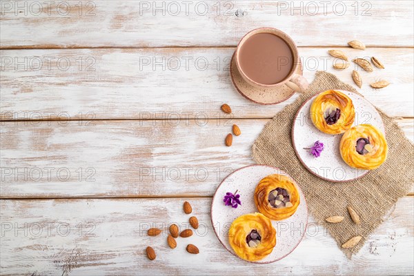 Small cheesecakes with jam and almonds with cup of coffee on a white wooden background and linen textile. top view, flat lay, copy space