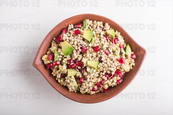 Salad of germinated buckwheat, avocado, walnut and pomegranate seeds in clay plate on white wooden background. Top view, close up