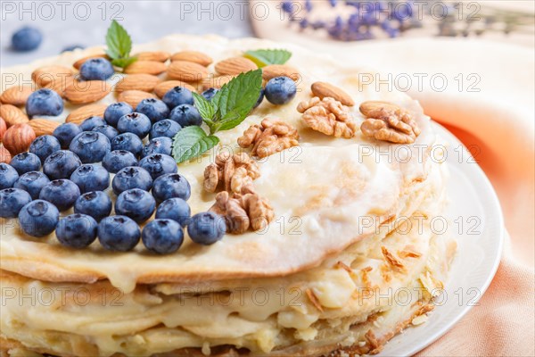 Homemade layered Napoleon cake with milk cream. Decorated with blueberry, almonds, walnuts, hazelnuts, mint on a gray concrete background. side view, selective focus, close up