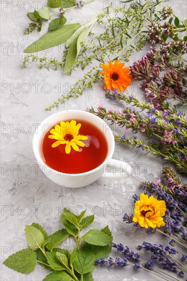 Cup of herbal tea with calendula, lavender, oregano, hyssop, mint and lemon balm on a gray concrete background. Morninig, spring, healthy drink concept. side view