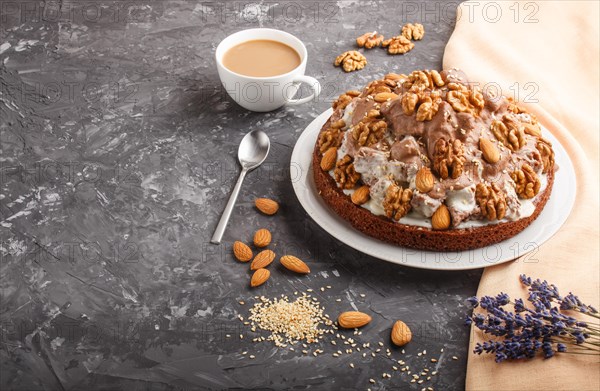 Homemade cake with milk cream, cocoa, almond, hazelnut on a black concrete background with orange textile and a cup of coffee. Side view, copy space