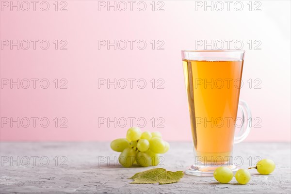 Glass of green grape juice on a gray and pink background. Morninig, spring, healthy drink concept. Side view, copy space