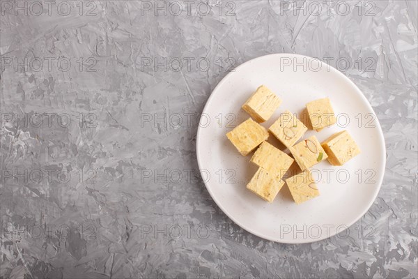 Traditional indian candy soan papdi in white plate with almond and pistache on a gray concrete background. top view, flat lay, copy space