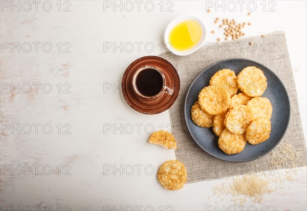 Traditional japanese rice chips cookies with honey and soy sauce on a blue ceramic plate and a cup of coffee on a white wooden background. Top view, flat lay, copy space