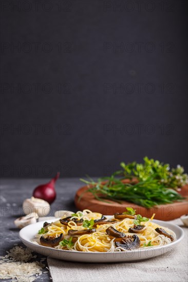 Rice noodles with champignons mushrooms, egg sauce and oregano on white ceramic plate on a black concrete background. side view, selective focus, copy space