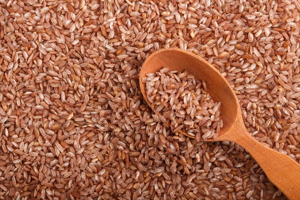 Texture of unpolished brown rice with wooden spoon. Top view, flat lay, close up, macro. Natural background