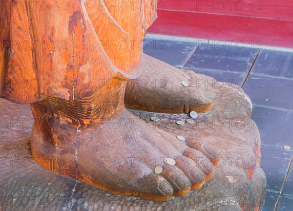 Coins laying on the feet of a wooden statue on top of plinth in South Korea