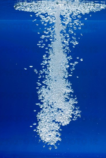 A thin jet of water penetrates the water surface and produces many air bubbles in the blue water of an aquarium