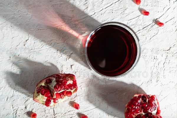 Glass of pomegranate juice on a white concrete background. Hard light, contrast. Top view, close up, flat lay