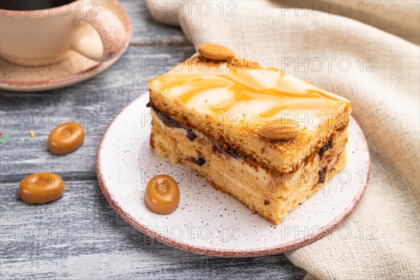 Honey cake with milk cream, caramel, almonds and a cup of coffee on a gray wooden background and linen textile. Side view, close up