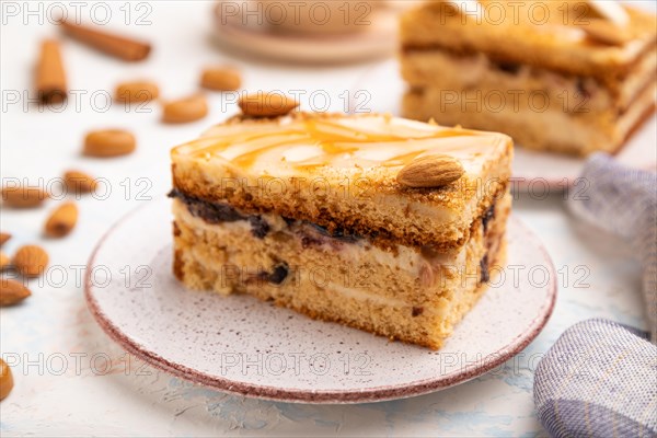Honey cake with milk cream, caramel, almonds and a cup of coffee on a white concrete background and linen textile. Side view, selective focus, close up