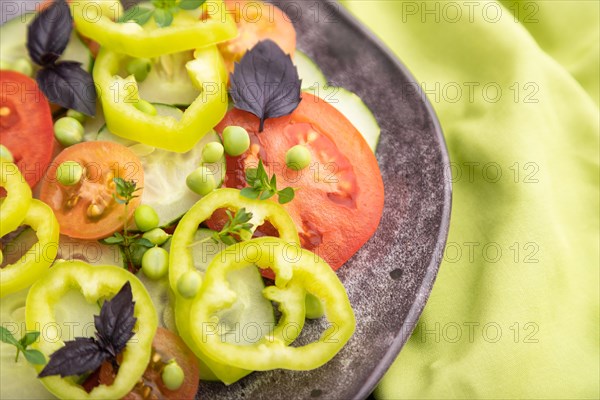 Vegetarian salad from green pea, tomatoes, pepper and basil on a green textile. Top view, close up, selective focus