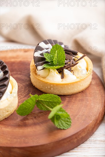 Sweet tartlets with chocolate and cheese cream with cup of coffee on a white wooden background and linen textile. side view, close up, selective focus