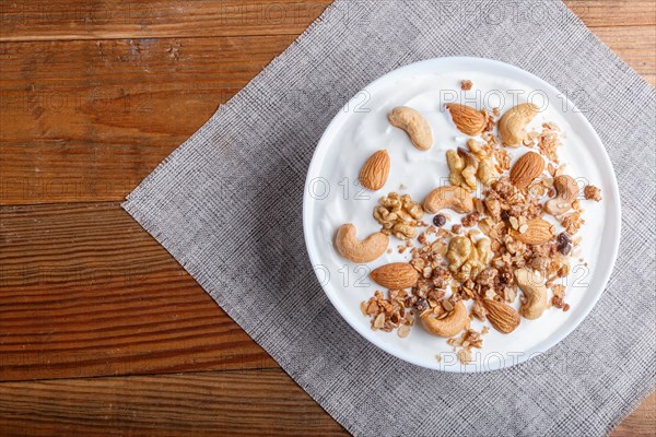 White plate with greek yogurt, granola, almond, cashew, walnuts on brown wooden background. top view. copy space