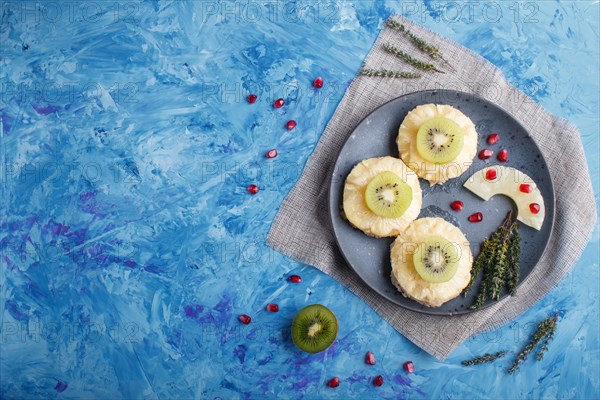 Pieces of baked pork with pineapple, cheese and kiwi on blue background, top view, copy space