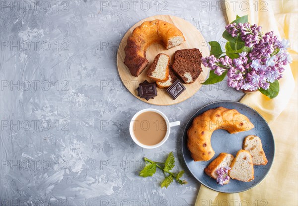 Cakes with raisins and chocolate and a cup of coffee. lilac flowers on a gray concrete background, top view, flat lay, copy space