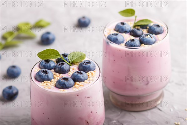 Yoghurt with blueberry and sesame in a glass and wooden spoon on gray concrete background. side view, close up