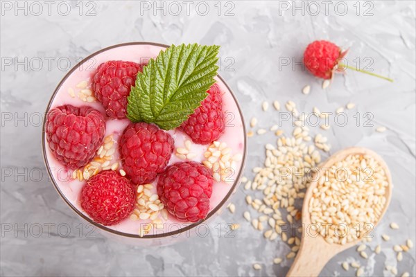 Yoghurt with raspberry and sesame in a glass and wooden spoon on gray concrete background. top view, flat lay, close up