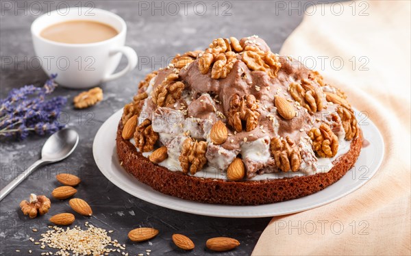 Homemade cake with milk cream, cocoa, almond, hazelnut on a black concrete background with orange textile and a cup of coffee. Side view, close up, selective focus