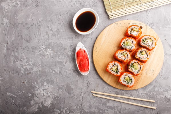 Japanese maki sushi rolls with flying fish roe, chopsticks, soy sauce and marinated ginger on wooden board on a gray concrete background. Top view, flat lay, copy space