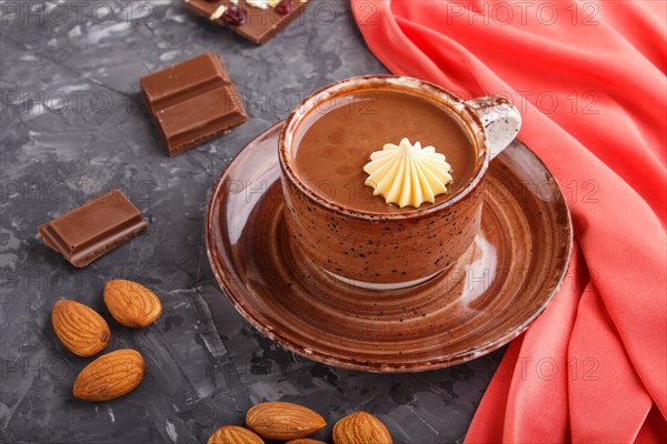 Cup of hot chocolate and pieces of milk chocolate with almonds on a black concrete background with red textile. side view, close up