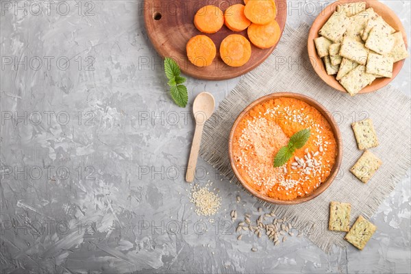 Carrot cream soup with sesame seeds and snacks in wooden bowl on a gray concrete background with linen textile. top view, flat lay, copy space