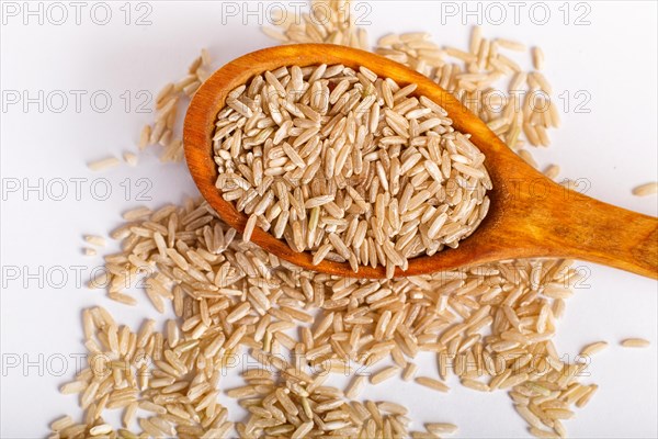 Pile of brown rice in a wooden spoon isolated on white background. Top view