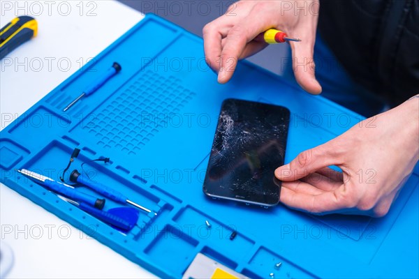 Top view close-up of the hands of a repairman opening a phone with a screwdriver in a workshop