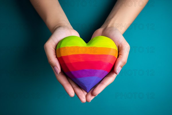 Top view of hands holding rainbow colored heart in front of blue background. KI generiert, generiert AI generated