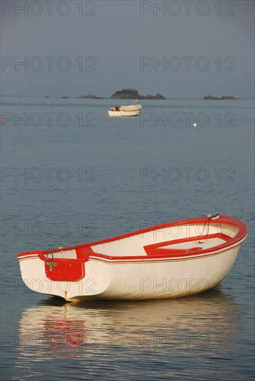 A lone red and white boat floats on a calm sea with the horizon in the background