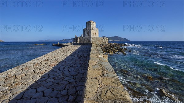 Stone path leads to a castle by the sea under a bright blue sky, octagonal medieval tower. Islet of Bourtzi, sea fortress of Methoni, Peloponnese, Greece, Europe