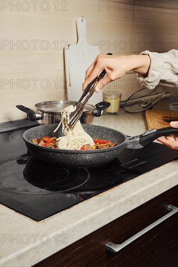 Unrecognizable woman moving cooked rice noodles into frying pan with vegetable dressing and beef