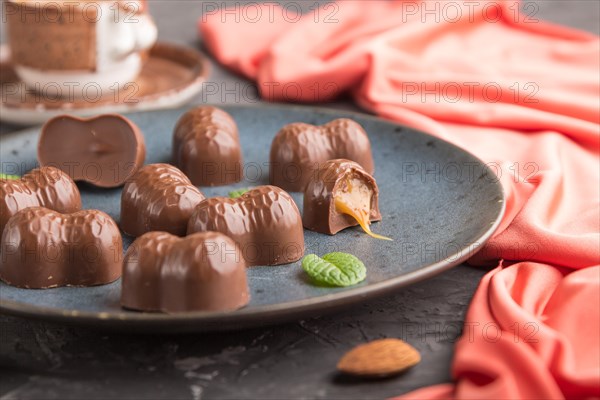 Chocolate caramel candies with almonds and a cup of coffee on a black concrete background and red textile. Side view, close up, selective focus