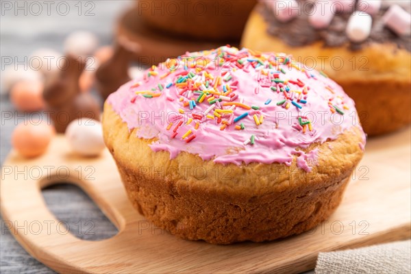 Homemade glazed and decorated easter pies with chocolate eggs and rabbits on a gray wooden background and linen textile. Side view, selective focus, close up