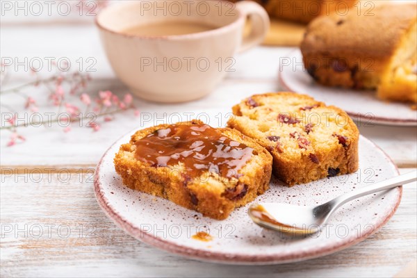 Homemade cake with raisins, almonds, soft caramel and a cup of coffee on a white wooden background. Side view, close up, selective focus