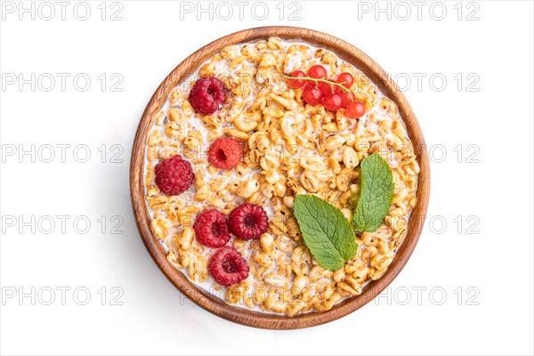Wheat flakes porridge with milk, raspberry and currant in wooden bowl isolated on white background. Top view, flat lay, close up