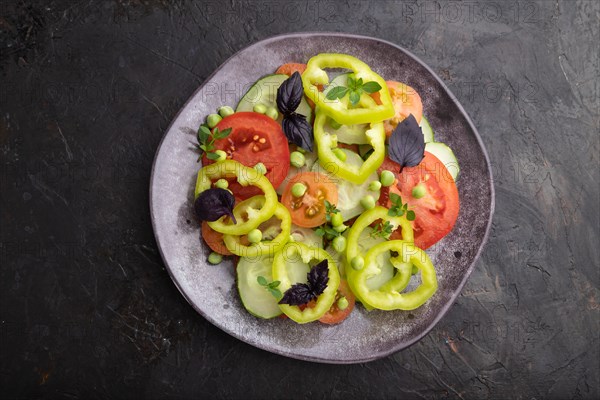 Vegetarian salad from green pea, tomatoes, pepper and basil on a black concrete background. top view, close up, flat lay