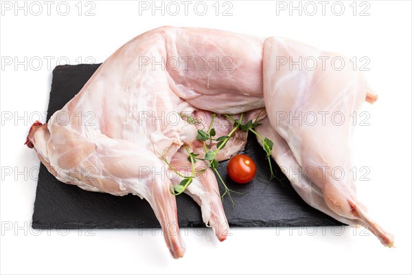 Whole raw rabbit with tomatoes, pea sprouts on a black concrete slate board isolated on white background. Side view, close up
